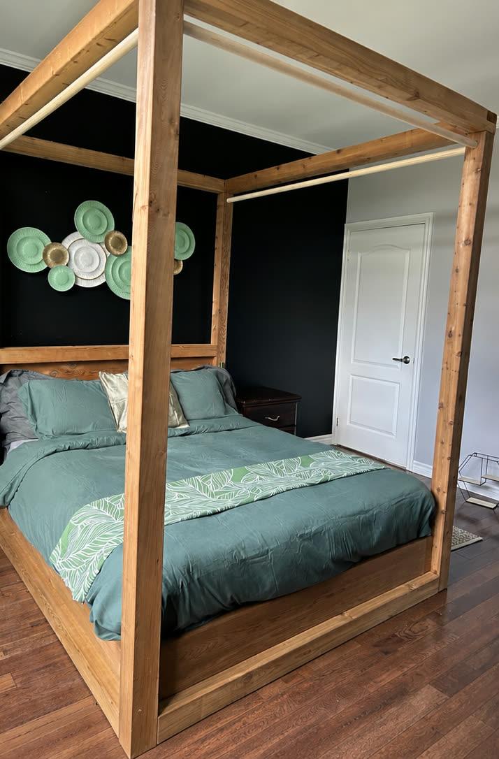 Chambre principale mise en scène avec lit à baldaquin en bois et literie verte.