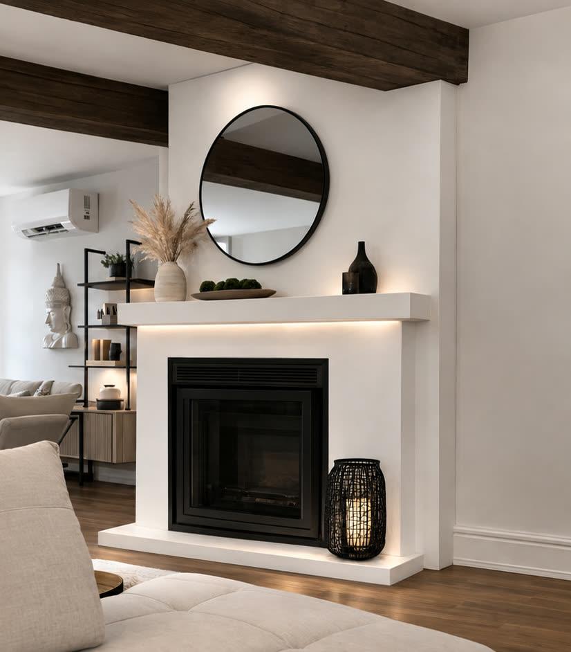 Salon avec foyer au manteau blanc sculptural, miroir rond et poutre de bois apparente.