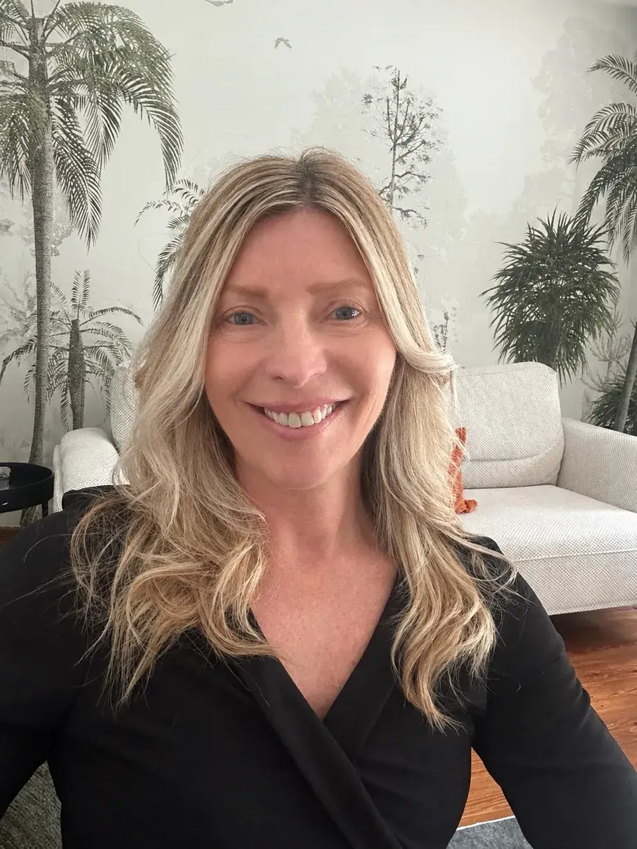 Portrait de la designer d’intérieur d’Expert Relooking, devant un mur peint de palmiers.